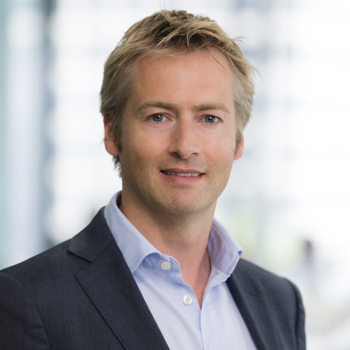 Professional corporate headshot photography of a male executive in Sydney A professional headshot of a male executive with blonde hair, wearing a dark suit jacket and light blue collared shirt, posing confidently in a bright Sydney office environment.