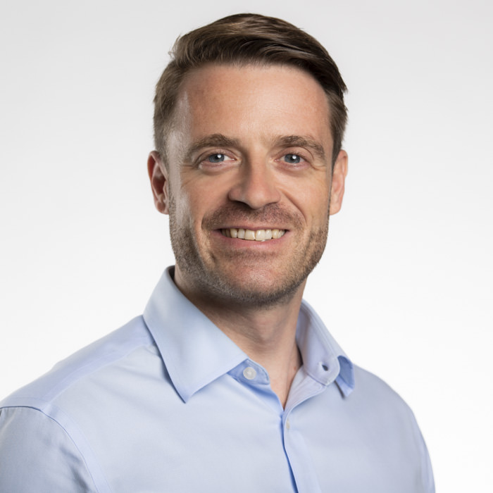 Professional corporate headshot photography of a male executive in Sydney A professional corporate headshot of a smiling male executive with neatly styled hair, wearing a light blue collared shirt, against a clean white background in a Sydney studio.
