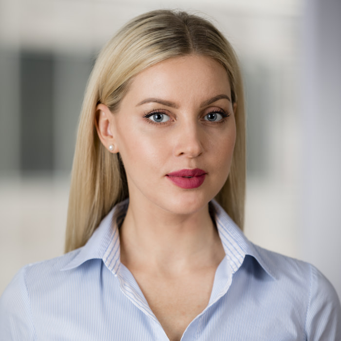 Professional headshot photography of a businesswoman in a Sydney office environment A professional headshot of a businesswoman with straight blonde hair, wearing a light blue collared shirt, posing confidently in a modern Sydney office setting.