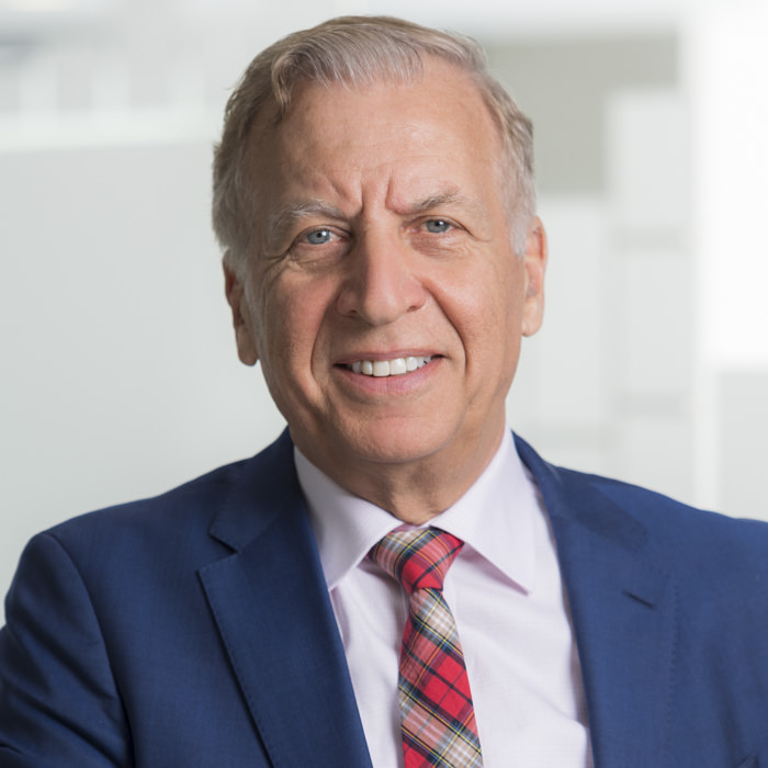 Professional corporate headshot photography of a senior executive in Sydney A professional corporate headshot of a senior executive wearing a blue suit, light pink shirt, and plaid tie, smiling confidently in a modern Sydney office setting.