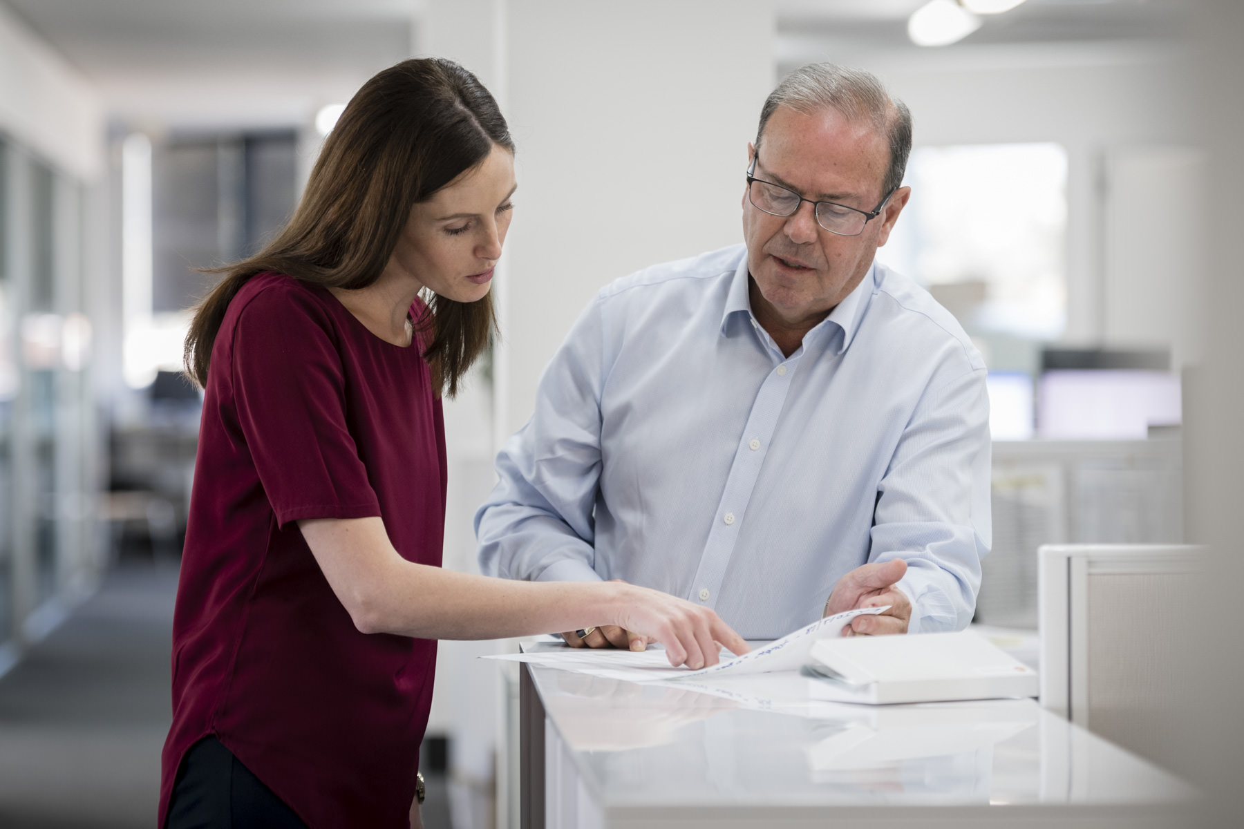 Corporate photography of colleagues collaborating in a Sydney office A corporate photograph of two colleagues discussing documents in a modern Sydney office, with a professional and focused atmosphere.